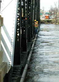 Two maintenance workers, hanging on the side of the bridge, inspect a bridge over the Minnesota River