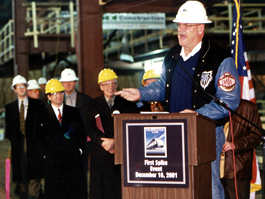 Governor at lectern people in hard hats behind him