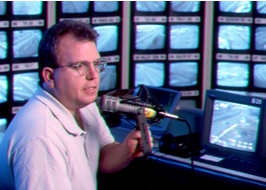 Man in front of microphone in with television screens surrounding him