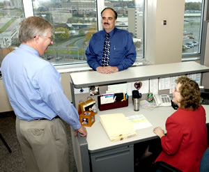 2 men standing at woman's desk