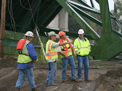 four men in safety gear under the collapsed 35W bridge
