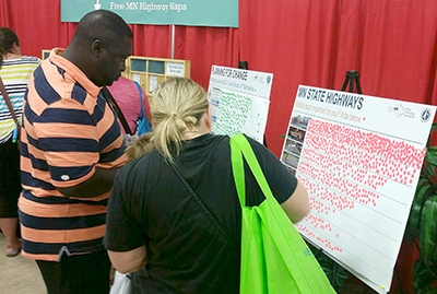 Photo of fairgoers placing stickers on poster boards at MnDOTs state fair booth.